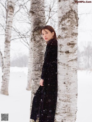 A woman leaning against a tree in the snow.