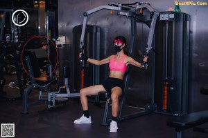A woman in a pink sports bra top and black gloves standing in front of a mirror.