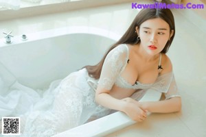 A woman in a white bra sitting in a bathtub.