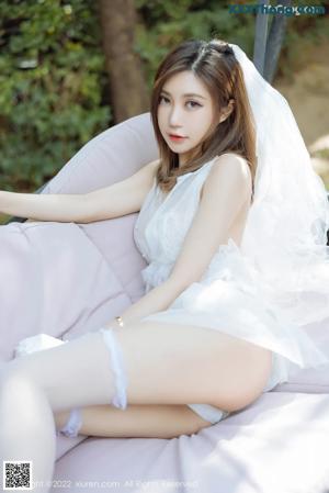 A woman in a white lingerie sitting on a bed.