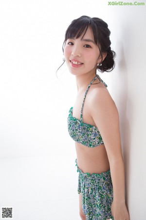 A woman in a bikini top and shorts leaning against a wall.