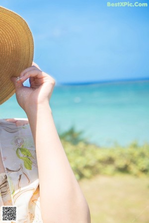 A naked woman in a straw hat sitting on a beach.