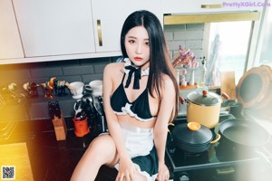 A woman in a black and white lingerie posing in a kitchen.