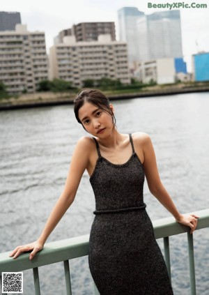 A woman in a black tank top leaning against a wall.