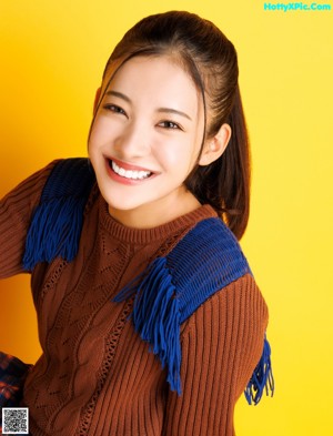 A woman wearing a brown sweater and a plaid skirt.