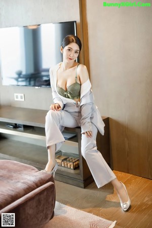 A woman in a green bra top and gray pants sitting on a couch.