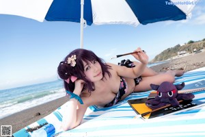 A woman in a bikini sitting under an umbrella on the beach.