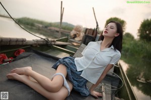A woman in a white shirt and plaid skirt sitting on a wooden dock.